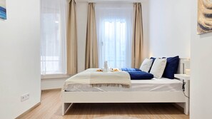 A modern bedroom with a white bed, beige curtains, and a view of the city. - IMCT - Central Vibe Apartments 3 (Budapest)