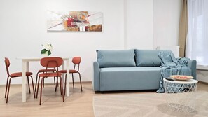 A modern living room with a light blue sofa, a dining table with chairs, and a painting on the wall. - IMCT - Central Vibe Apartments 3 (Budapest)