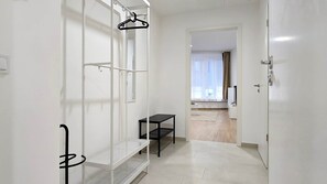 A hallway with a white door, a black bench, a white shelf, and a black hanger. - IMCT - Central Vibe Apartments 3 (Budapest)