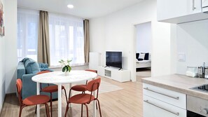 A modern living room with a sofa, a dining table with chairs, a TV, and a kitchenette. - IMCT - Central Vibe Apartments 3 (Budapest)