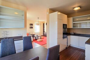 Una cucina moderna con mobili bianchi, un'area pranzo con tappeto rosso e un soggiorno con divano e lampadario.