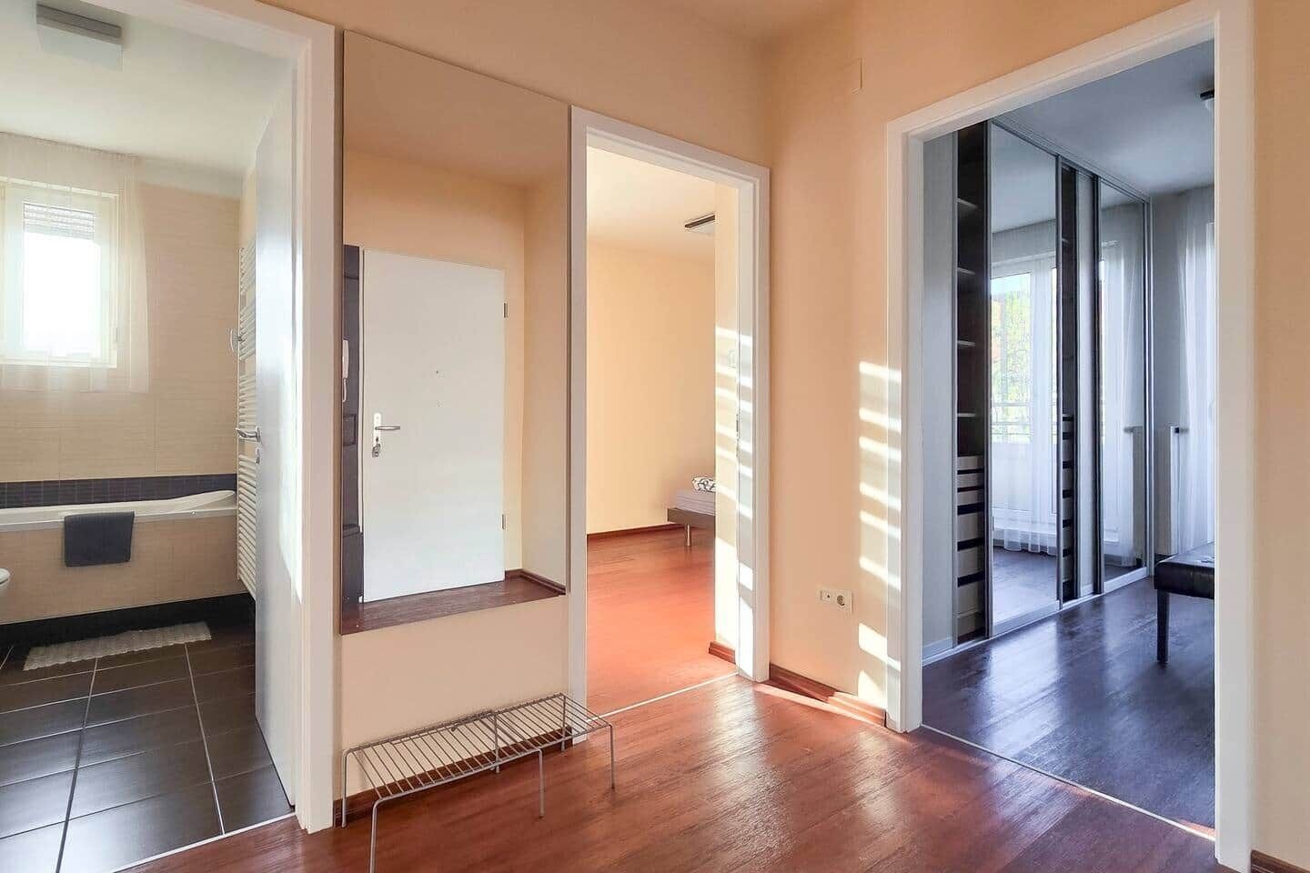 Um corredor com uma porta que dá para um banheiro, um banco e vista para uma varanda.