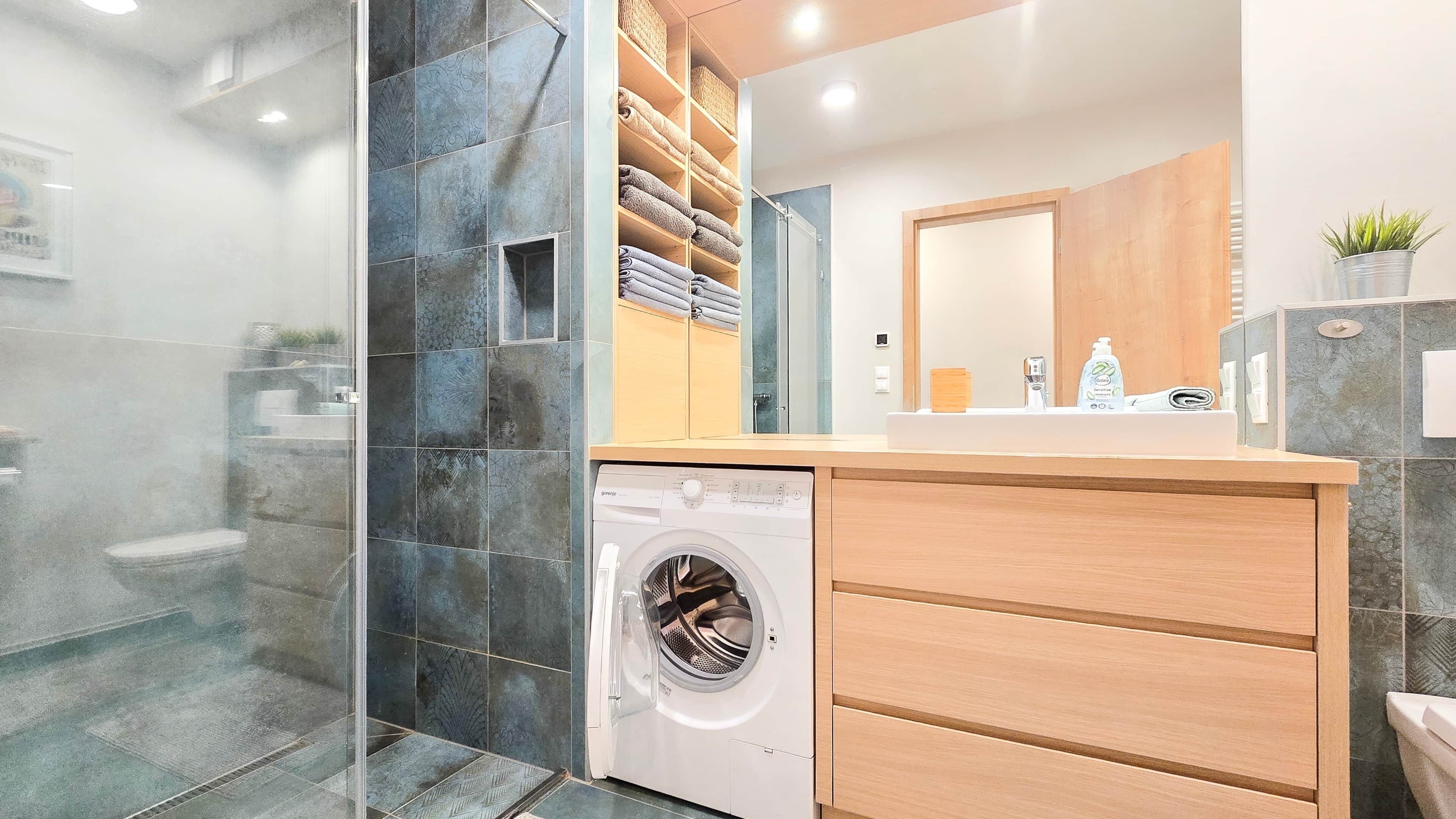 Ein modernes Badezimmer mit integrierter Waschmaschine, einem Holz-Waschtisch und einer Duschkabine aus Glas.