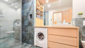Ein modernes Badezimmer mit integrierter Waschmaschine, einem Holz-Waschtisch und einer Duschkabine aus Glas.