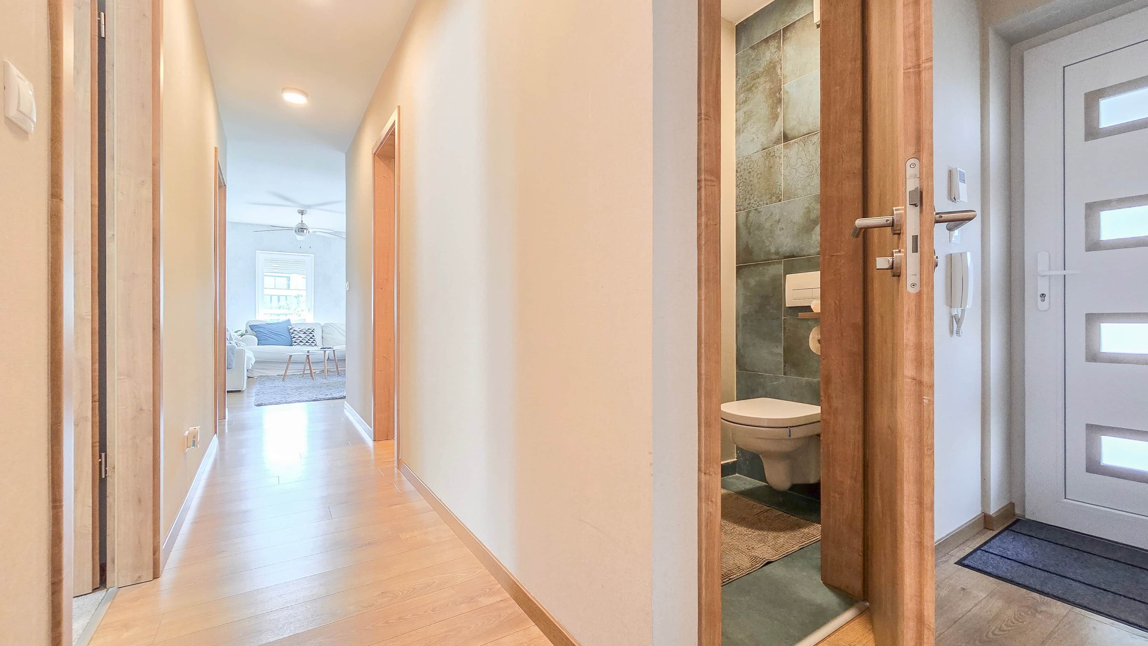 A hallway with wooden flooring leading to a bathroom with a toilet and a shower area.