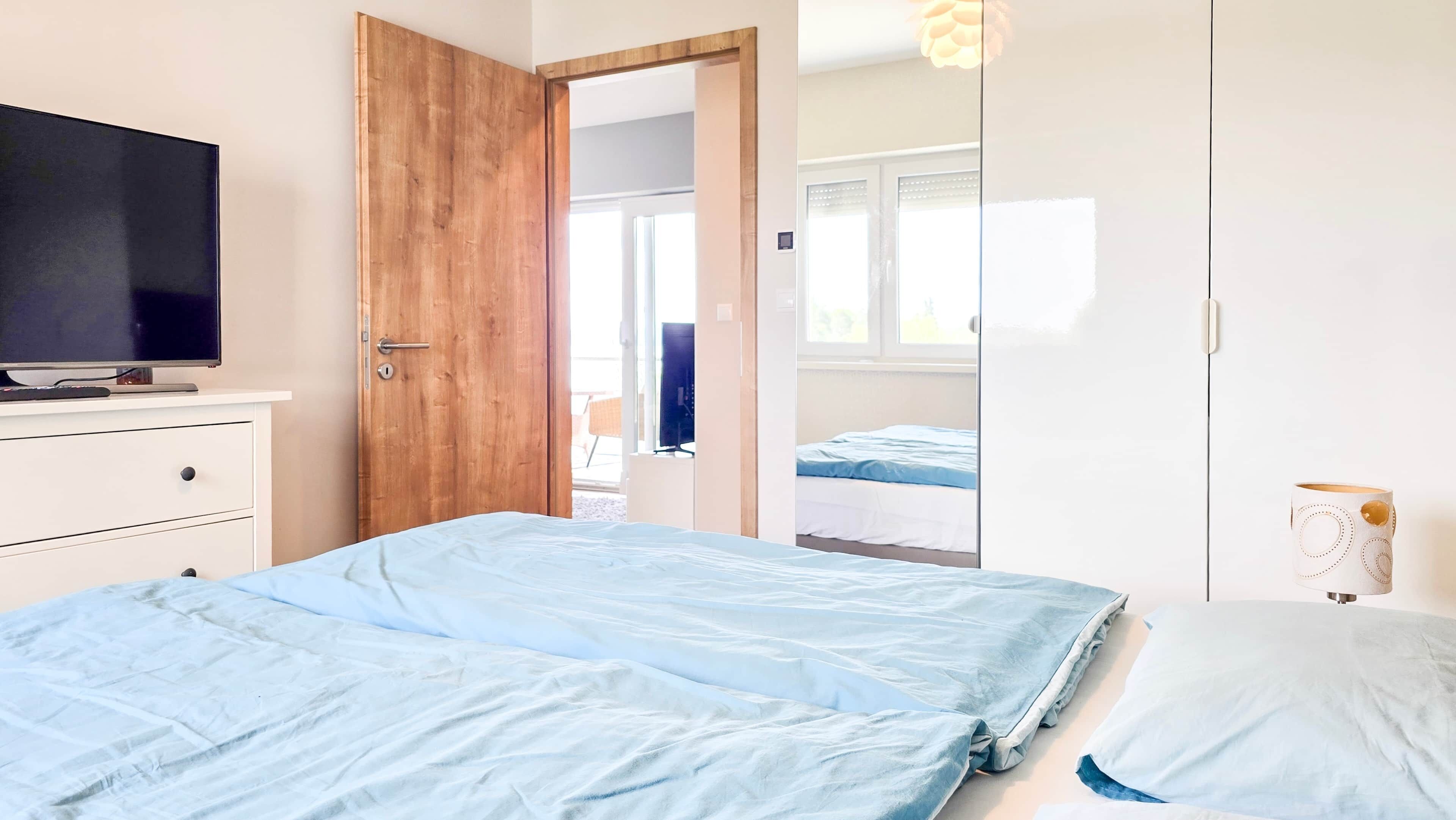 A bedroom with a bed, a TV on a dresser, and a door leading to another room.
