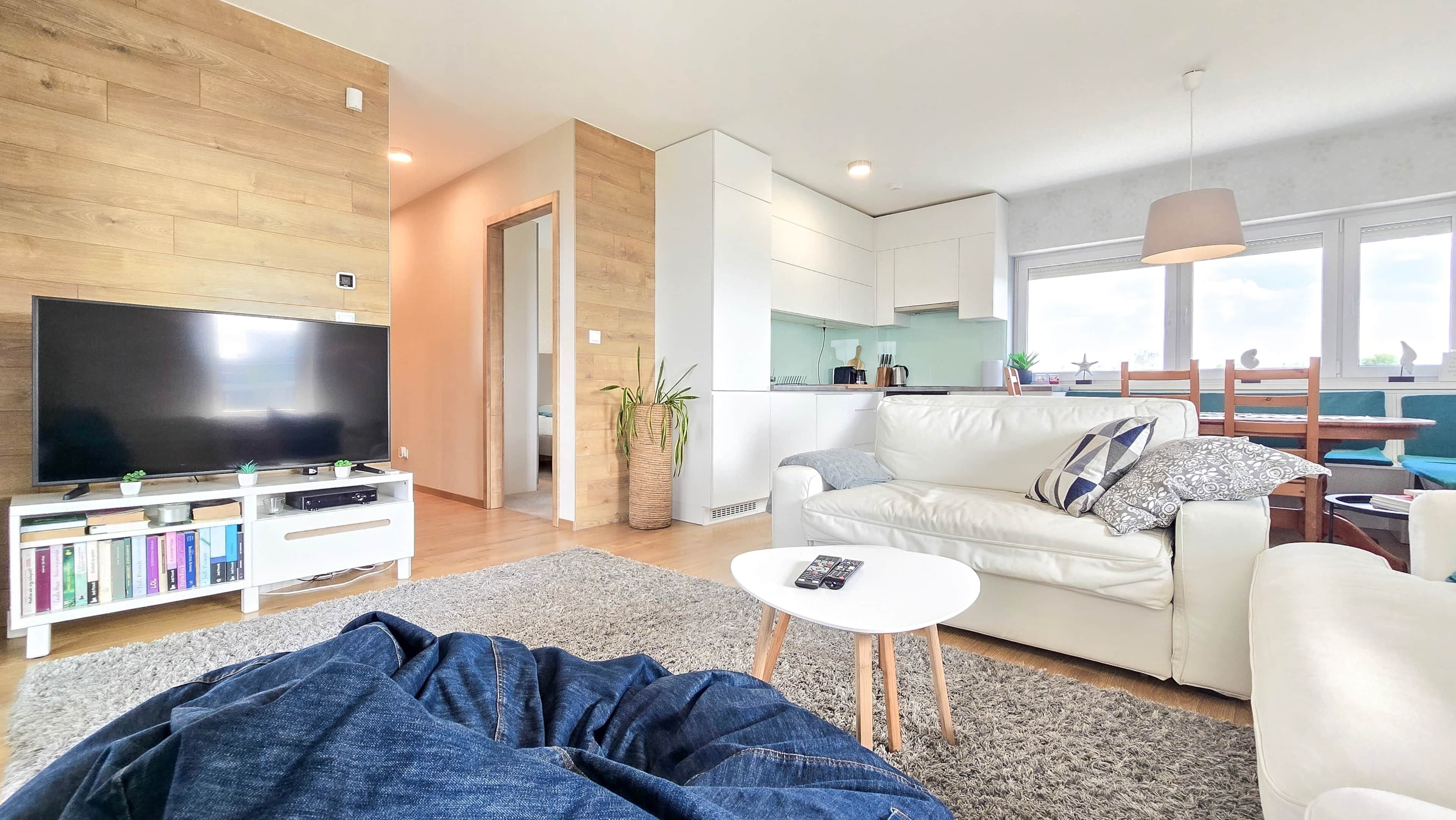 A modern living room with a flat-screen TV, a white sofa, a coffee table, and a bookshelf.