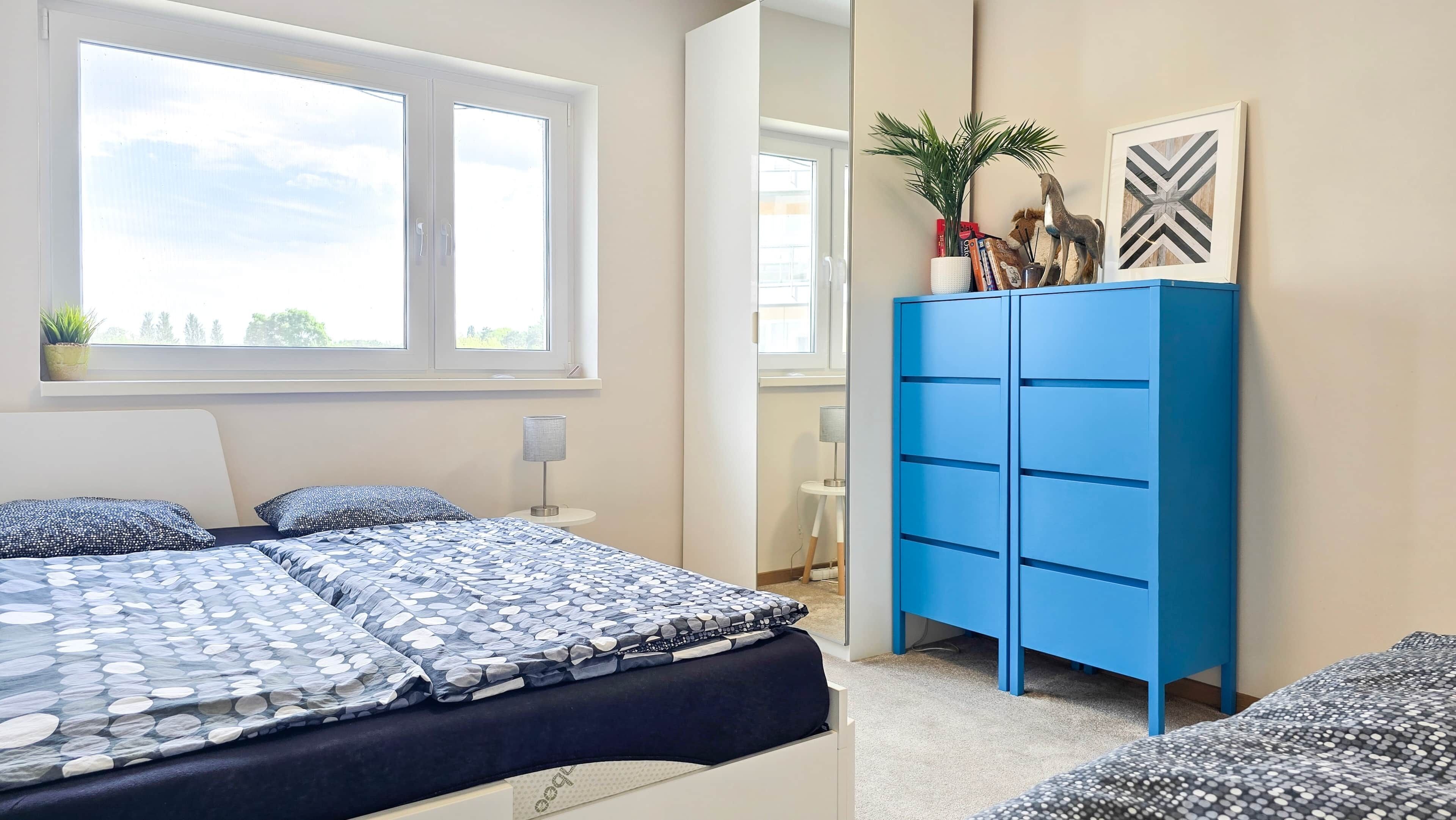 A bedroom with a bed, a wardrobe, a window, and a plant.