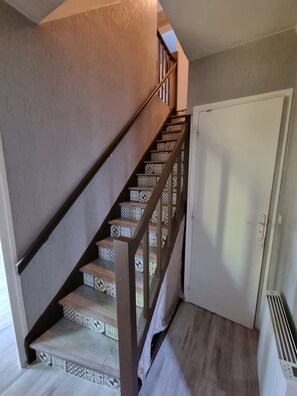 Una escalera con peldaños estampados que conduce a un rellano, una puerta con marco blanco y una rejilla en la pared.