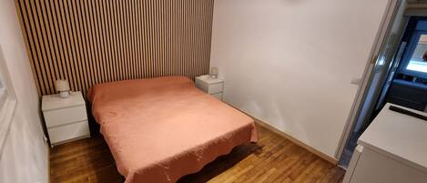 A bedroom with a bed, a nightstand, a lamp, a wooden slat wall, and a small cabinet.