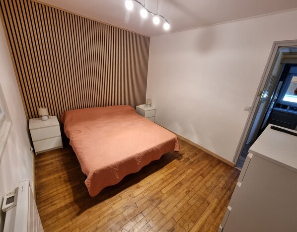 Un dormitorio con cama, mesita de noche, lámpara, pared de listones de madera y un armario pequeño.
