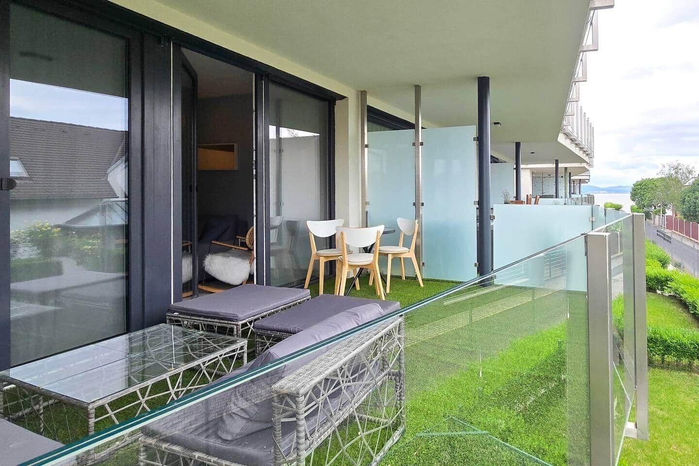 Un balcon avec une table en verre, deux chaises et un canapé.