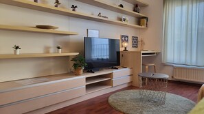 A modern living room with a flat-screen TV, wooden shelves, and a round coffee table. - IMCT - Passage Apartman (Budapest)