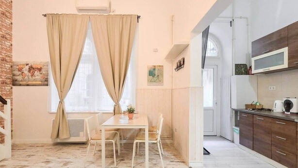 A room with a dining table, chairs, a potted plant, and a kitchen area with cabinets and a microwave. - IMCT - MSpirit Apartman A Budapest (Budapest)