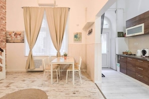 Ein Zimmer mit Esstisch, Stühlen, einer Zimmerpflanze und einer Küchenzeile mit Schränken und einer Mikrowelle.
