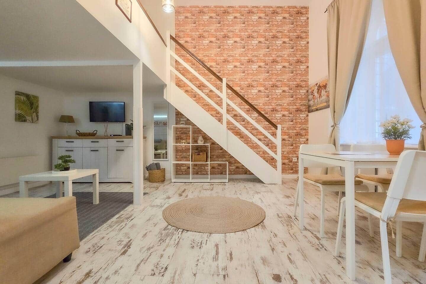 A modern living room with a staircase, a dining area, and a kitchen in the background.