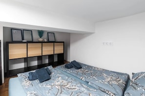 A bedroom with a bed, a nightstand, a dresser, and a wall-mounted shelf with framed pictures. - IMCT - Rose Apartment mini (Budapest)