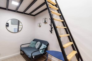 Et værelse med en blå sofa, et rundt spejl, en stige og et lille bord med en plante.