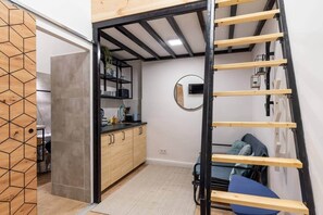 A compact room with a kitchenette, a bed with a headboard, and a small seating area. - IMCT - Rose Apartment mini (Budapest)