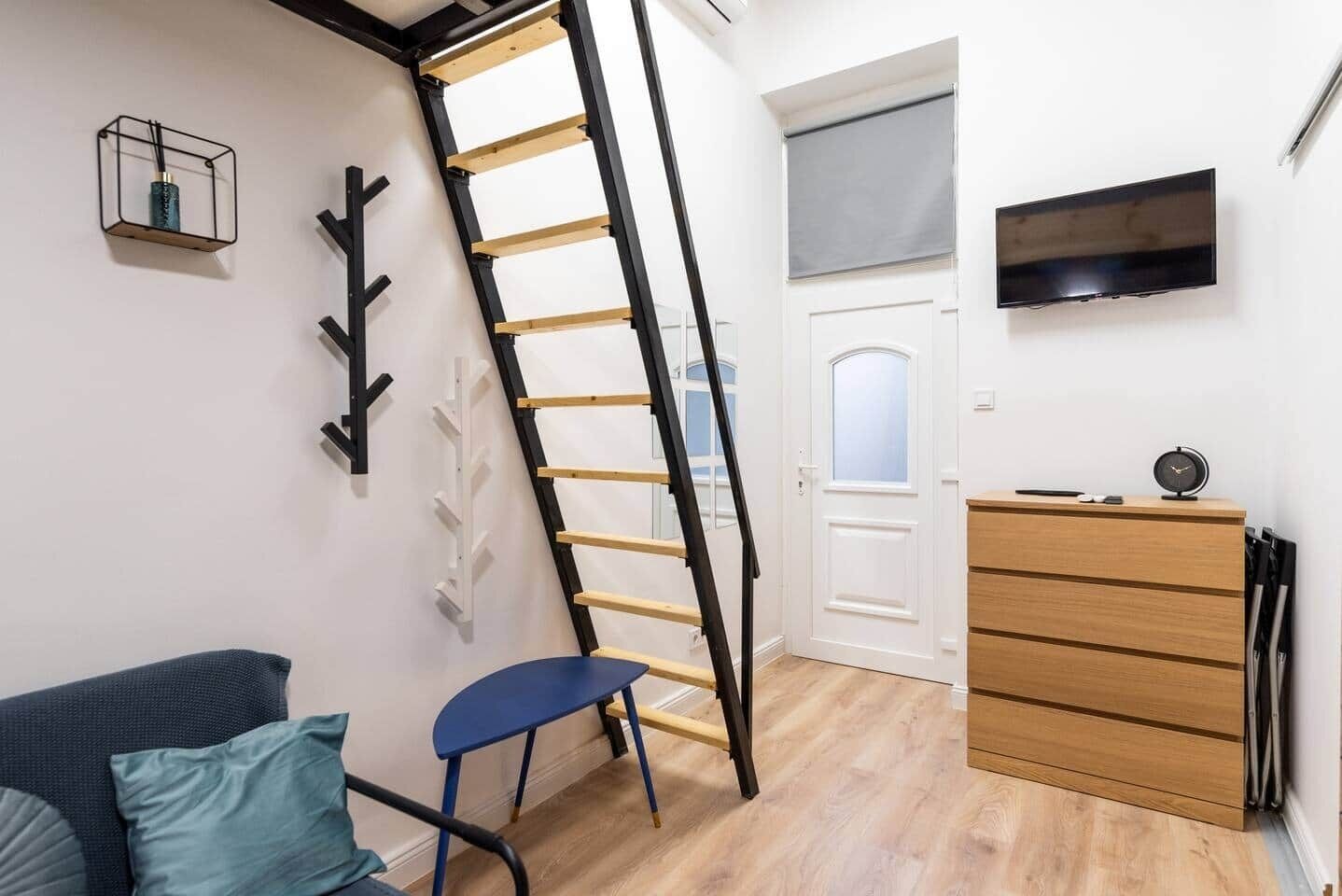 A room with a wooden ladder, a TV mounted on the wall, a wooden dresser, and a chair.
