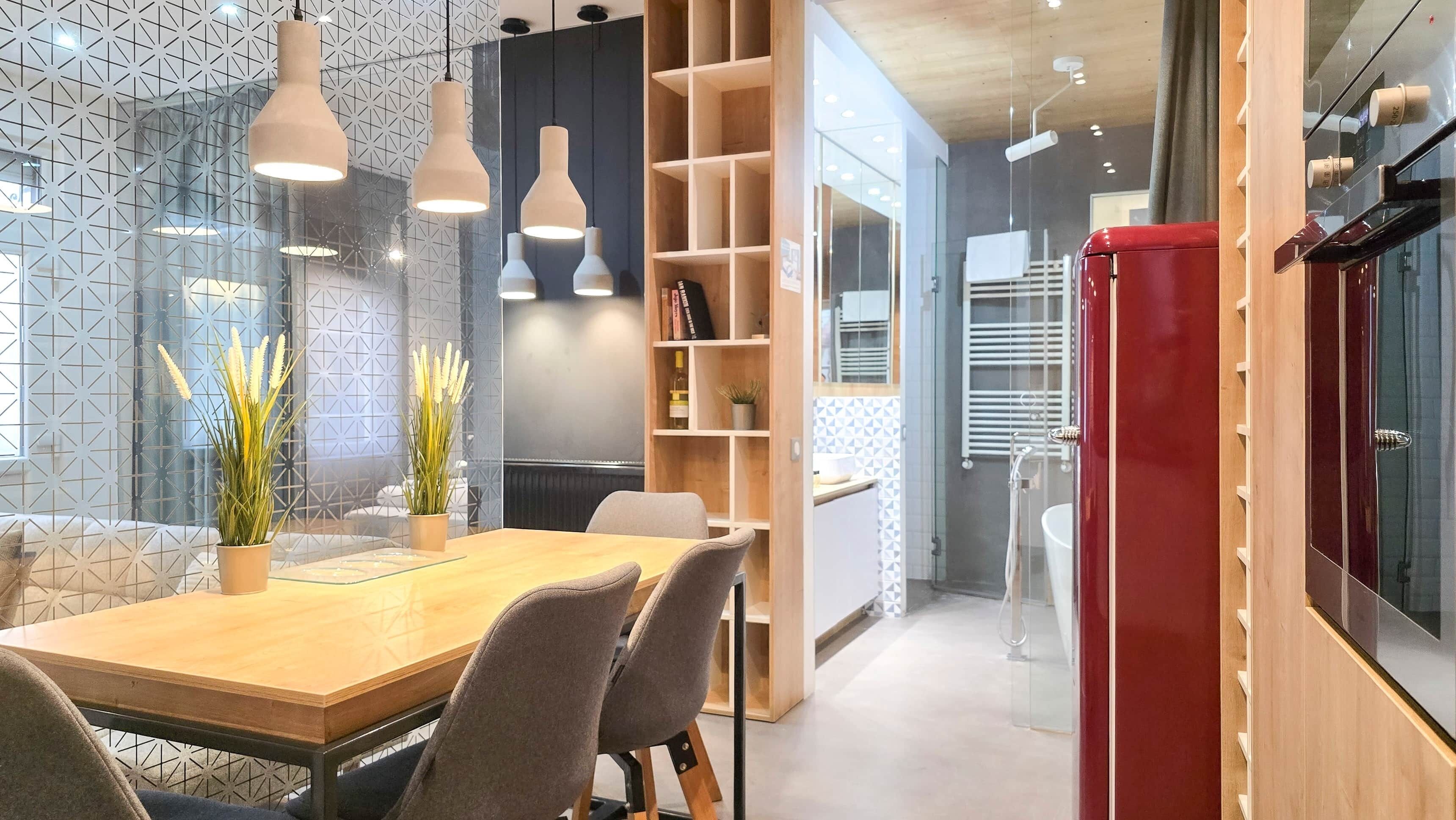 Un intérieur moderne avec un coin repas, des étagères en bois et des luminaires suspendus.