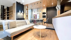 A modern living room with a sofa, a coffee table, and a dining area with chairs and a table. - IMCT- WOODnest Home with A/C (Budapest)