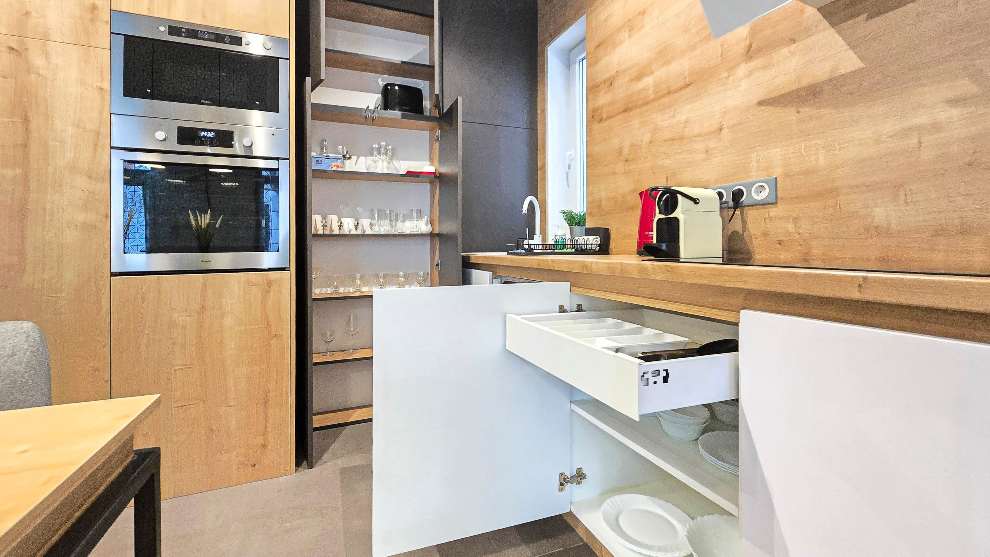 A modern kitchen with built-in appliances, a wooden wall, and a countertop with a sink and storage.