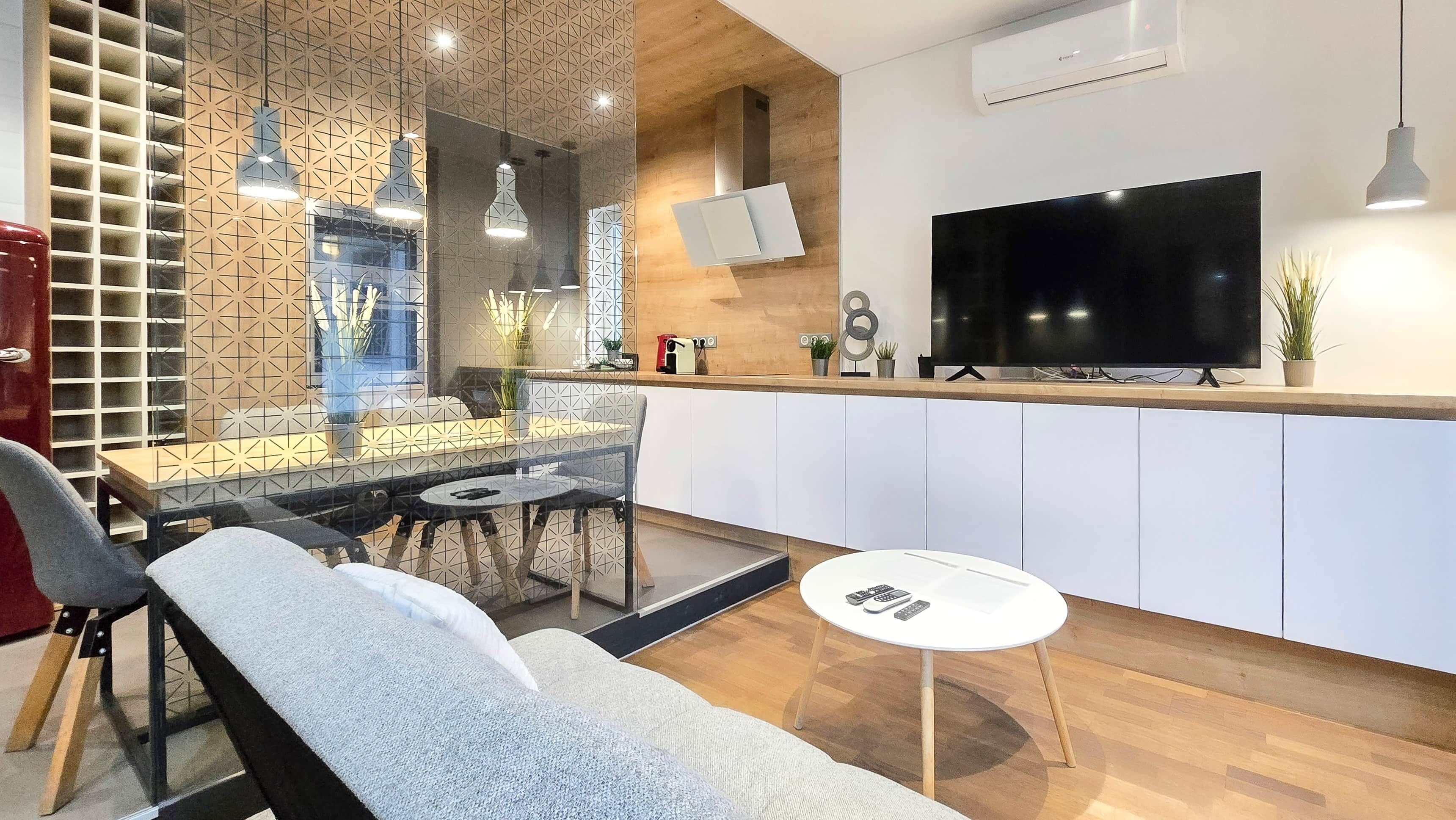 A modern living room with a sofa, a dining table, and a TV mounted on the wall.