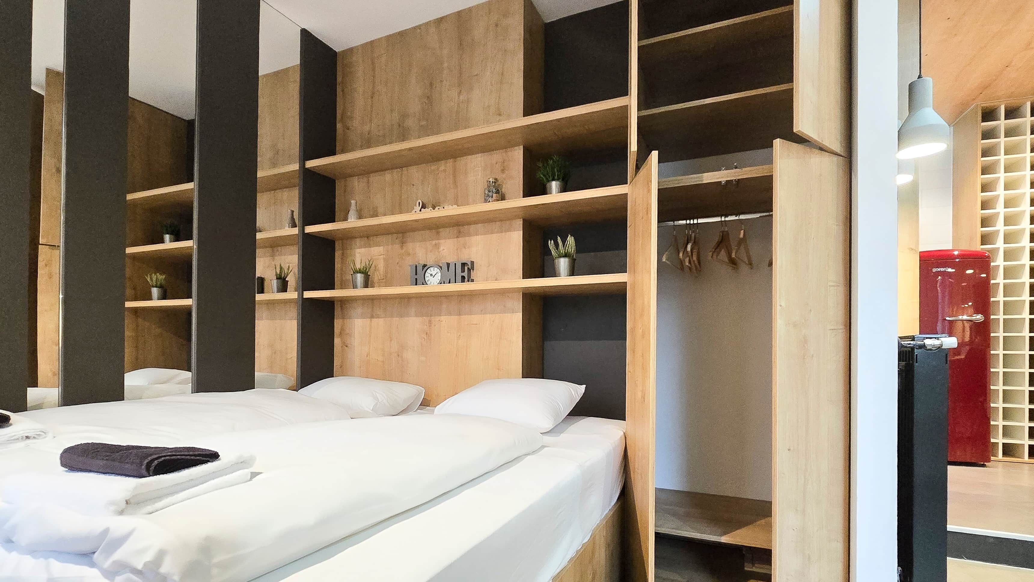 Une chambre avec deux lits, des étagères en bois ornées de plantes, une armoire rouge et un porte-serviettes mural.