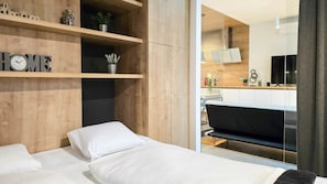 A modern bedroom with a bed, wooden shelving, and a view of a kitchen area. - IMCT- WOODnest Home with A/C (Budapest)