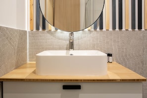 Ein Badezimmer mit einem rechteckigen Waschbecken, einem Spiegel darüber und einer Holzauslage.