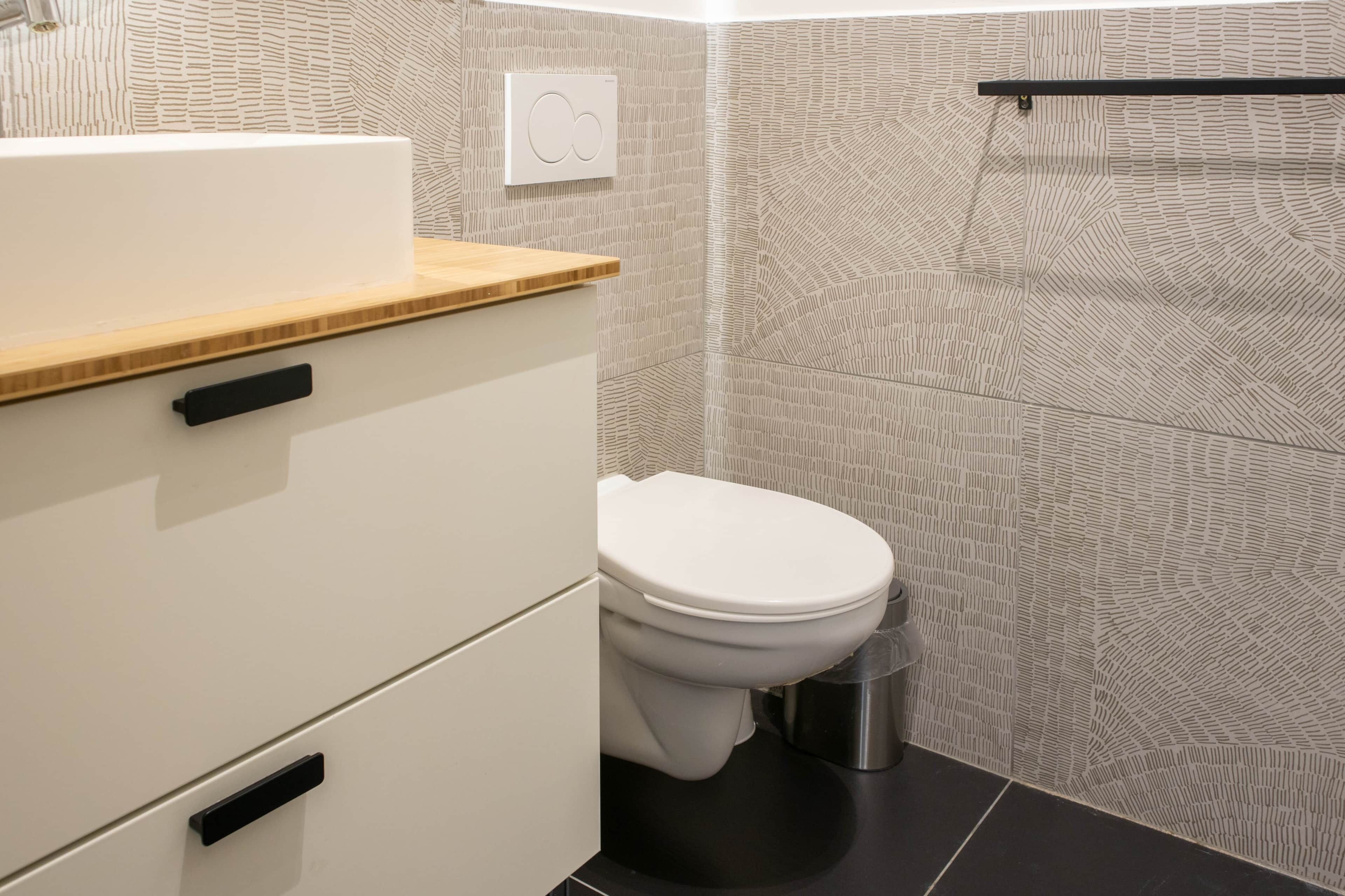 Une salle de bain moderne avec des toilettes, un lavabo doté d’un plan de travail en bois et un mur orné d’un motif.