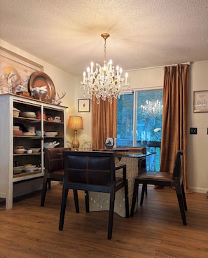 Ein Esszimmer mit einer Chandelierleuchte, Holzsesseln, einem Tisch und Blick durch ein Fenster.