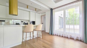 A modern kitchen with white cabinets, a stainless steel oven, and a bar area with two stools. - IMCT - Sun Hill A211 Luxury Suites (Budapest)