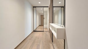 A narrow hallway with wooden flooring, a white bench, and a mirrored closet door. - IMCT - Sun Hill A211 Luxury Suites (Budapest)