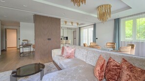 A modern living room with a large sofa, a glass coffee table, and a dining area visible in the background. - IMCT - Sun Hill A211 Luxury Suites (Budapest)