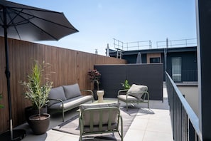 A balcony with a sofa, two chairs, a small table, and a potted plant.