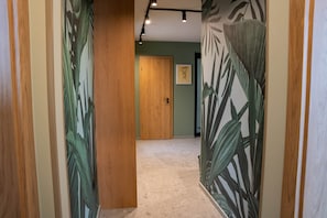 A hallway with wooden doors, a green wall, and a framed artwork on the wall. - IMCT - Urban Jungle Apartments 06 (Budapest)