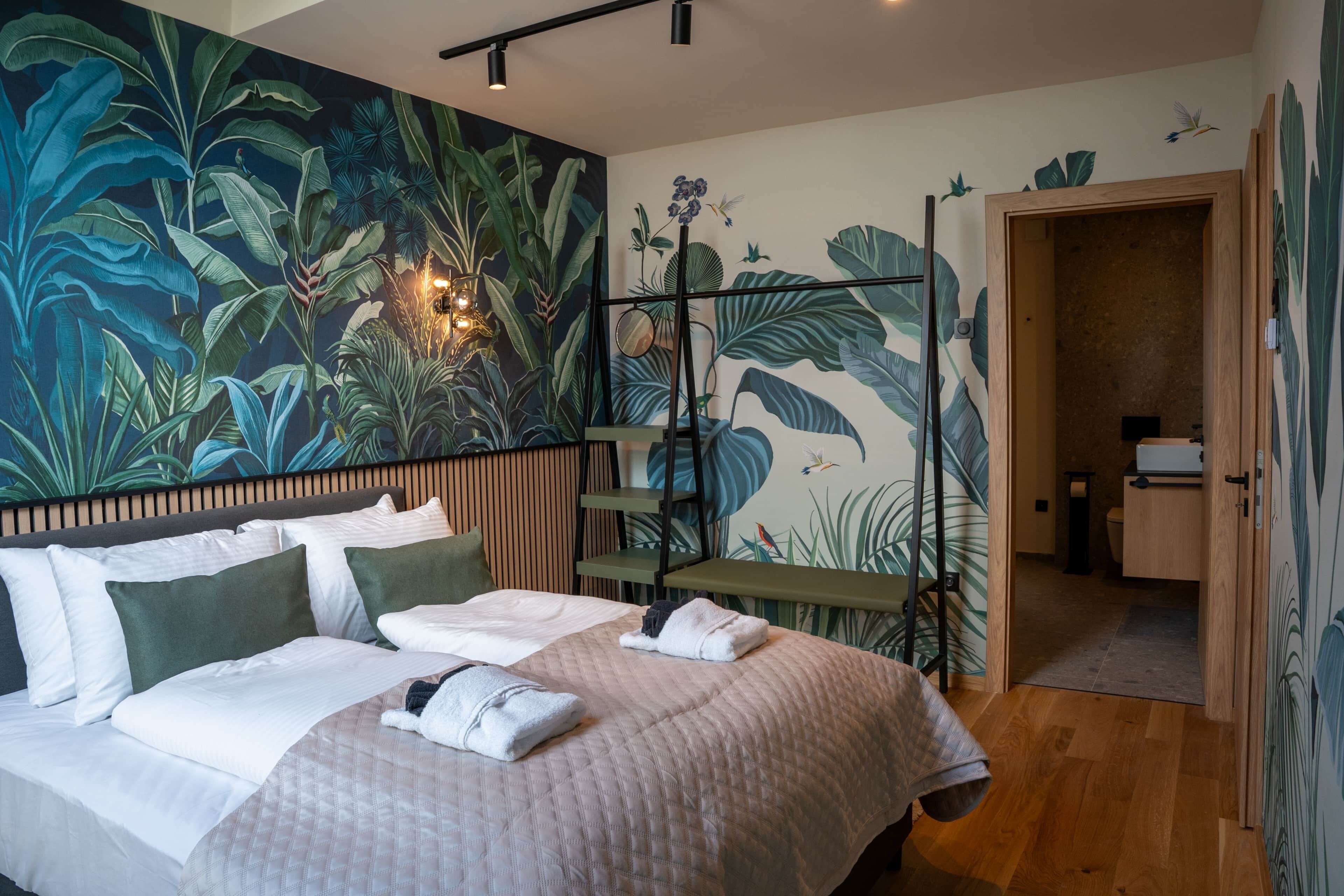 A bedroom with a bed, pillows, a nightstand, a wall-mounted lamp, and a door leading to a bathroom.