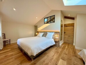 A bedroom with a large bed, a wooden floor, a skylight, a wooden door, and a nightstand with a lamp. - Le Clos des Rosiers - Maison de charme (Fouras)