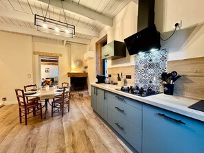 A modern kitchen with a central island, wooden dining table, and chairs. - Le Clos des Rosiers - Maison de charme (Fouras)