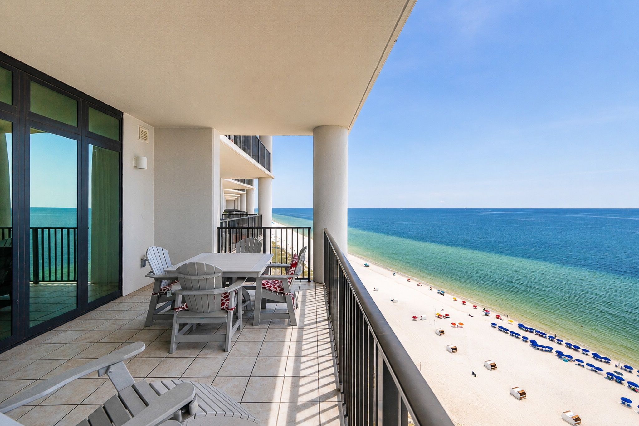 A balcony with a table and chairs, overlooking a beach with umbrellas.