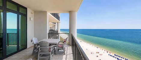 A balcony with a table and chairs, overlooking a beach with umbrellas.