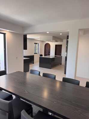 Een moderne keuken met donkere kastjes, een centraal eiland en een eethoek met een grote tafel en stoelen.