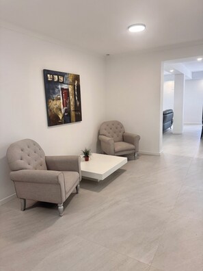 Een moderne woonkamer met twee beige fauteuils, een witte salontafel en een abstract kunstwerk aan de muur.