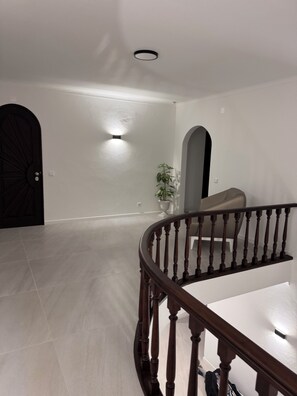 A spacious interior with a wooden staircase, a potted plant, and a black door. - Villa Irene 7 Bed Villa close to Marina (Vilamoura)
