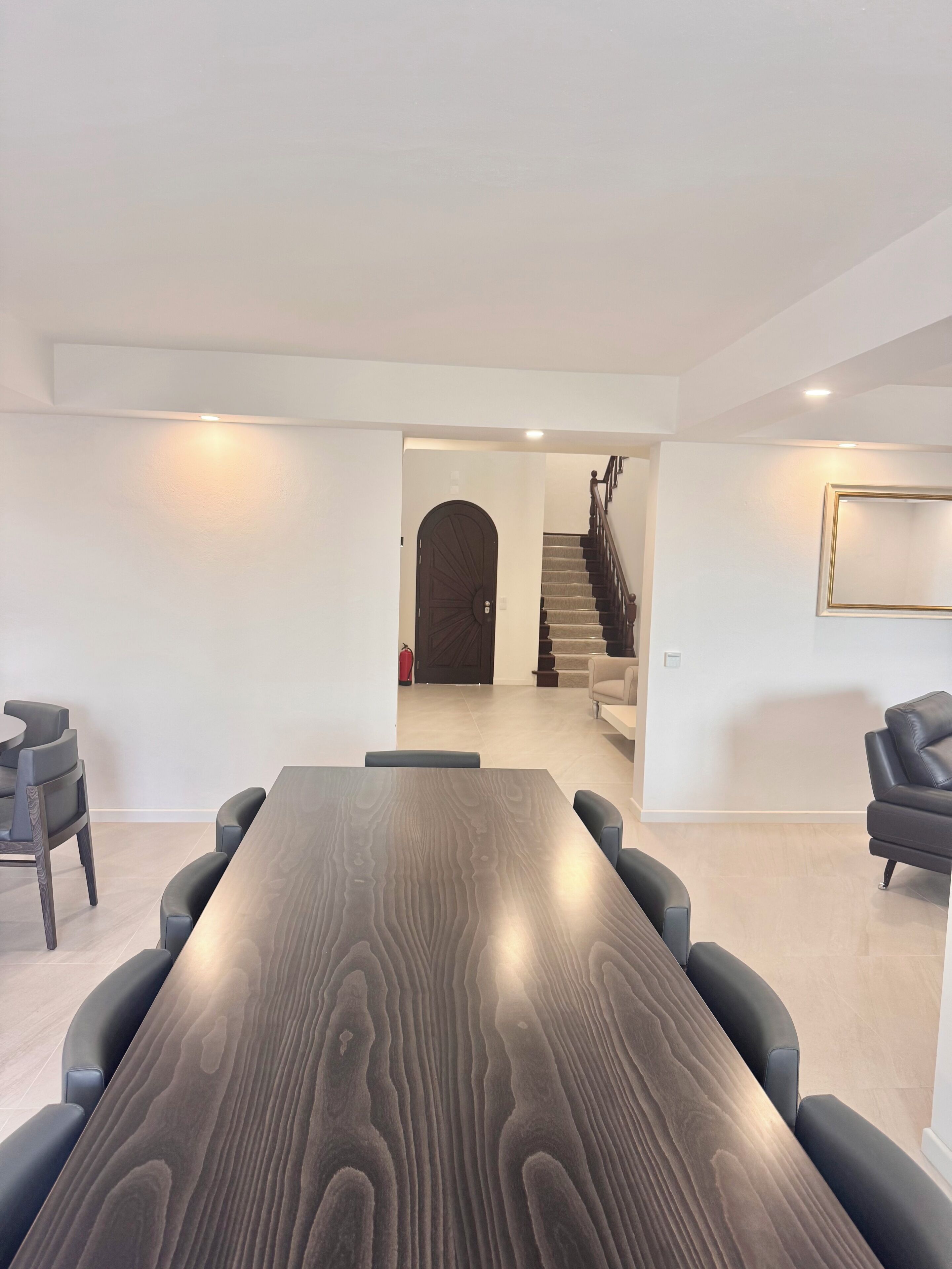 Ein modernes Interieur mit einem langen Holztisch, schwarzen Stühlen, einer Treppe und einem gerahmten Bild an der Wand.