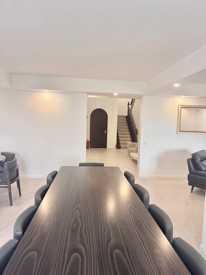 Een modern interieur met een lange houten tafel, zwarte stoelen, een trap en een ingelijst kunstwerk aan de muur.