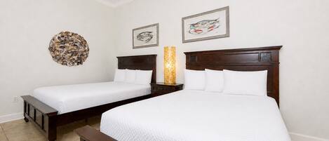 A hotel room with two beds, a nightstand, a wall-mounted lamp, and framed artwork.