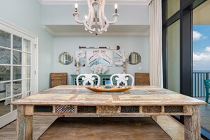 Une table à manger au design rustique, entourée de chaises, d’un lustre et d’œuvres d’art murales sur le thème de la marine.